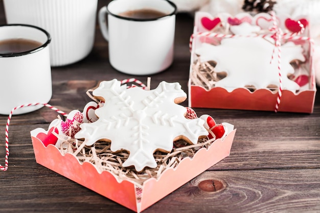 Gingerbread snowflakes with icing in open boxes and two mugs of tea on a wooden table. Christmas treat