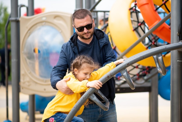 A girl 6-7 years old with her dad on the playground.