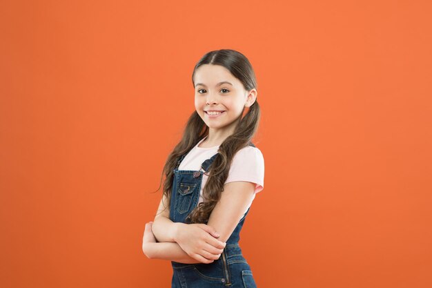 Girl adorable kid stand over orange background What is key to childhood happiness Happy childhood Grow mentally and physically healthy child Wellbeing and health Childhood concept Fashion girl