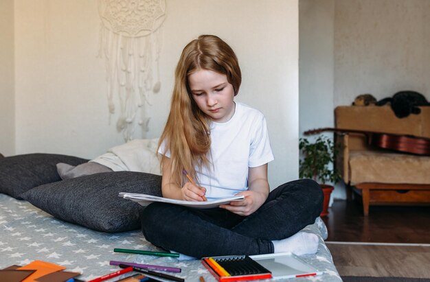 Photo the girl after school plays at home draws with pencils and felt-tip pens