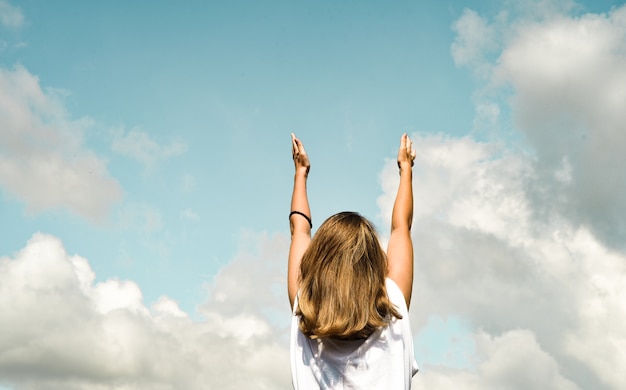 girl against the blue sky, stands with her back and pulls her hands up.