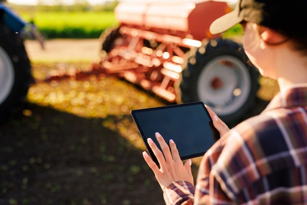 Photo a girl agronomist with a tablet manages agribusiness against the background of a tractor