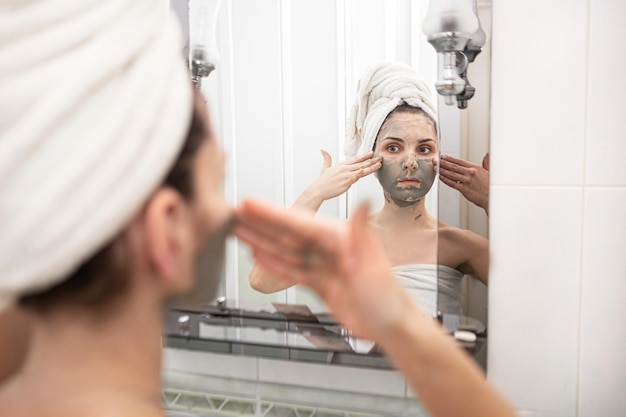 The girl applies a mask of black clay for skin health in the bathroom.