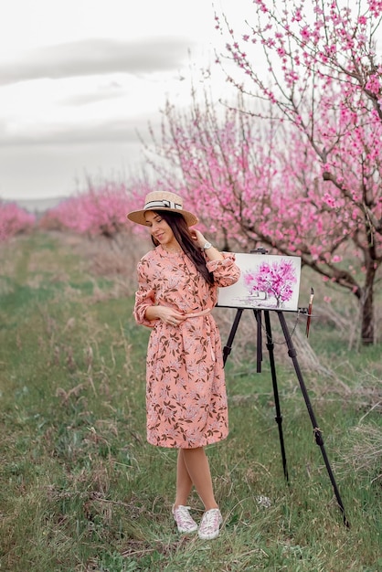 Girl artist paints a peach orchard in a peach orchard spring