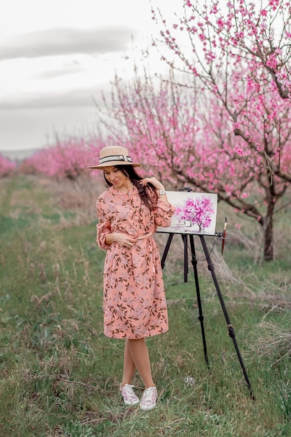 Girl artist paints a peach orchard in a peach orchard spring