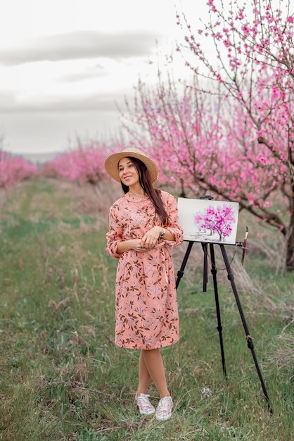 Girl artist paints a peach orchard in a peach orchard spring