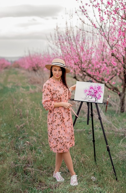 Girl artist paints a peach orchard in a peach orchard spring