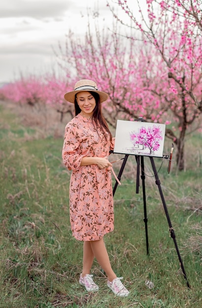 Girl artist paints a peach orchard in a peach orchard spring