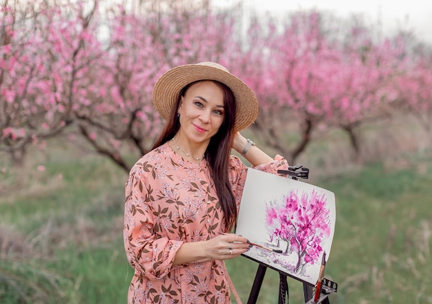 Girl artist paints a peach orchard in a peach orchard spring