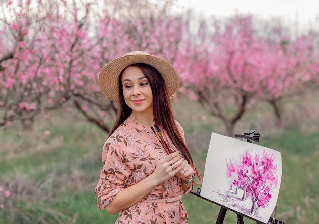 Girl artist paints a peach orchard in a peach orchard spring