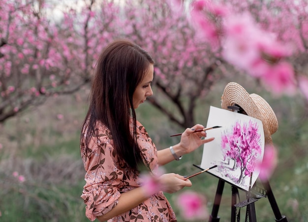 Girl artist paints a peach orchard in a peach orchard spring