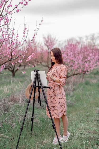 Girl artist paints a peach orchard in a peach orchard spring