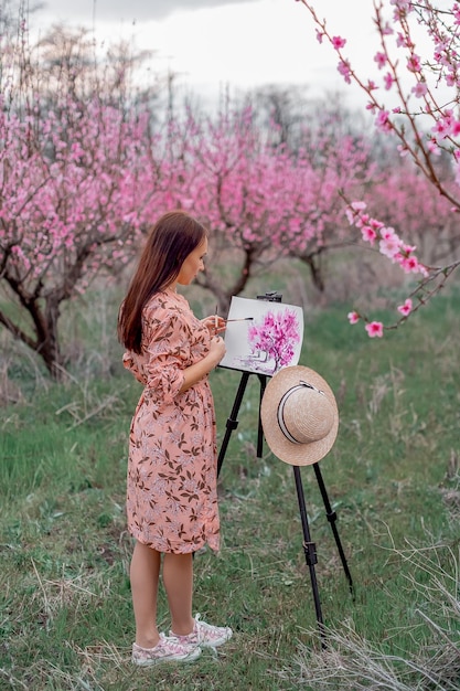 Girl artist paints a peach orchard in a peach orchard spring