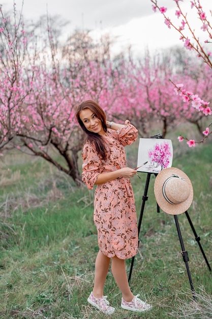 Girl artist paints a peach orchard in a peach orchard spring