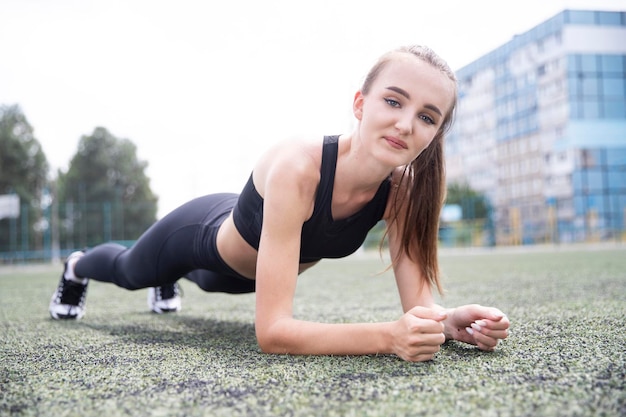 Girl athlete doing sports plank exercises at the stadium Outdoor sports