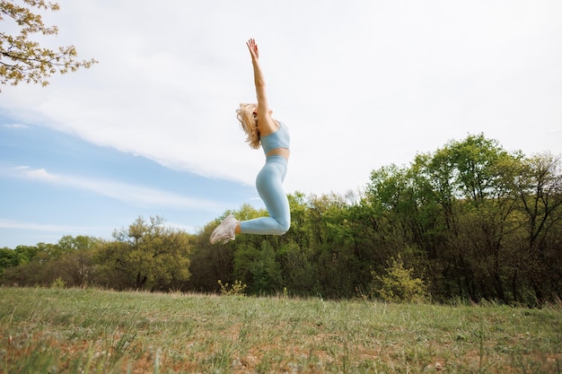 A girl athlete jumps up in the park Beautiful blonde Caucasian woman in blue tight tracksuit