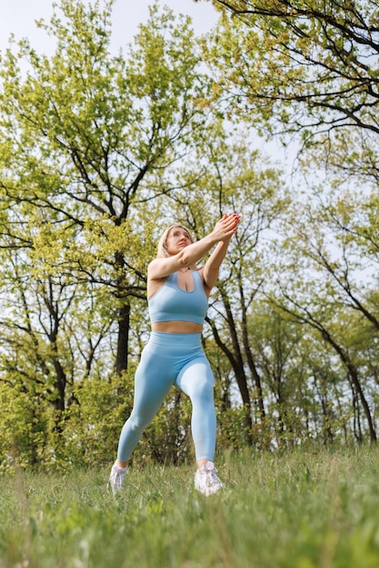 Girl athlete training in the park stretched her arms in front of her and performs lunges forward