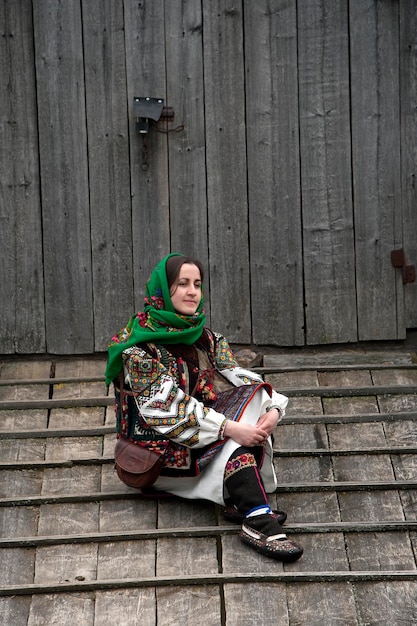 A girl in an authentic national hutsul costume sits on the floor near the barn door