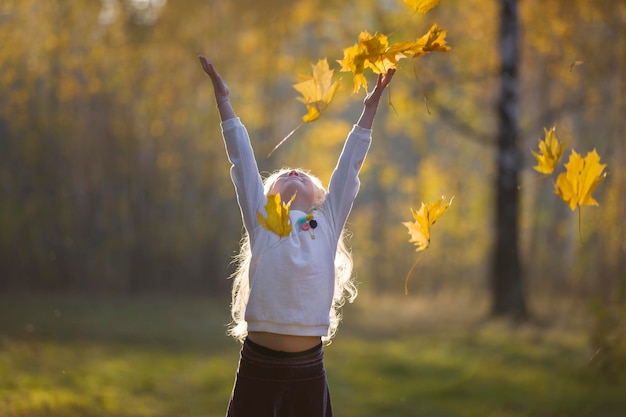 A girl in the autumn park scatters maple leaves A child on a walk in the fall