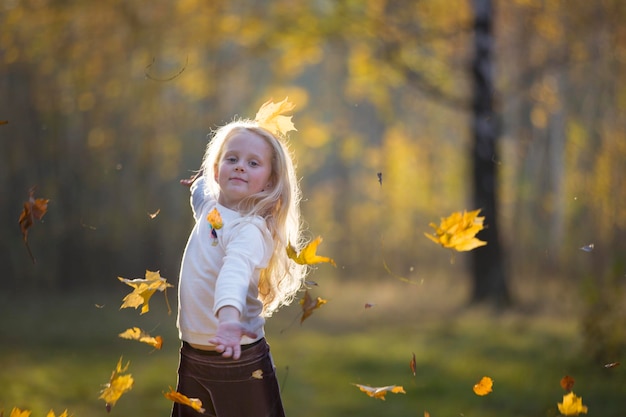 A girl in the autumn park scatters maple leaves A child on a walk in the fall