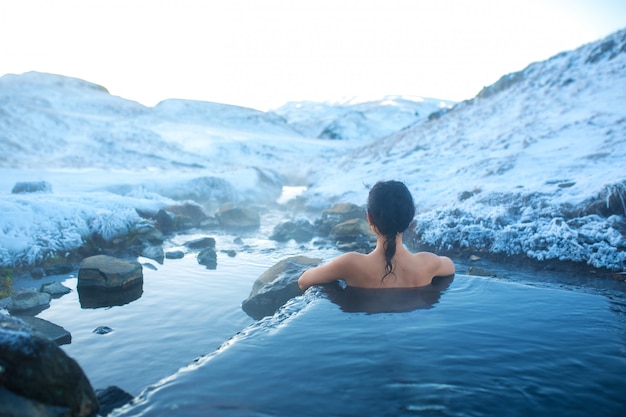 The girl bathes in a hot spring in the open air with a gorgeous view of the snowy mountains. Incredible iceland in winter