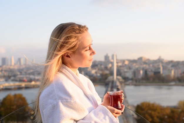 A girl in a bathrobe with a cup of Turkish tea at sunrise on the terrace of a house 