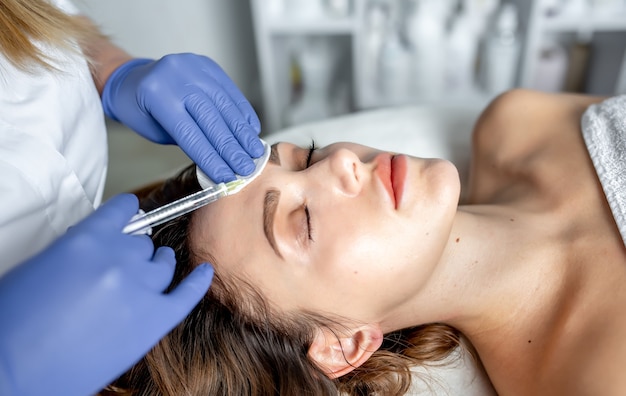 Girl beautician makes injections on the lips and face of a beautiful woman in a cosmetic wedge. Cosmetology concept.