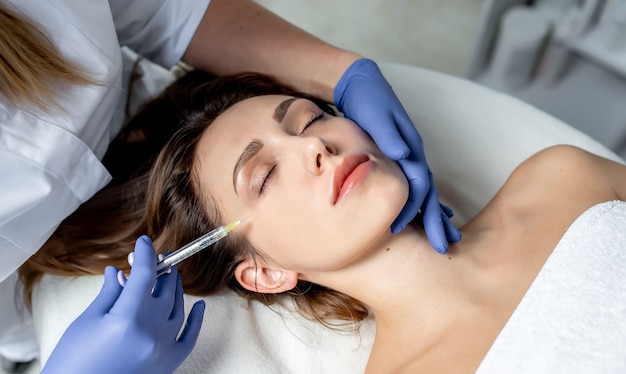 Girl beautician makes injections on the lips and face of a beautiful woman in a cosmetic wedge