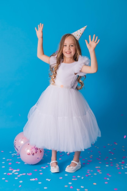 girl in a beautiful dress and a cardboard hat stands on a blue background and throws confetti