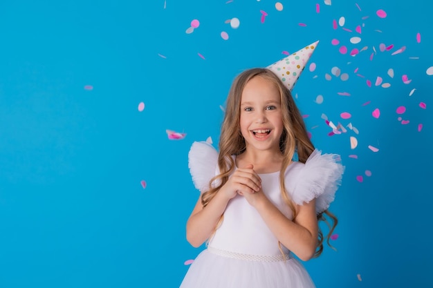 girl in a beautiful dress and a cardboard hat stands on a blue background and throws confetti