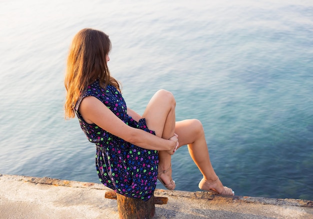 The girl in a beautiful dress is sitting on the pier