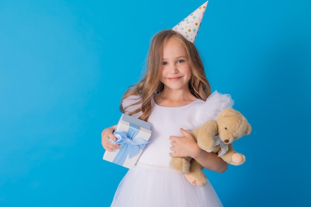 girl in a beautiful fluffy white dress holds a teddy bear and a gift box in her hands