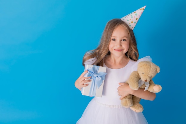 girl in a beautiful fluffy white dress holds a teddy bear and a gift box in her hands