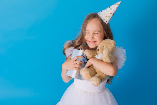 girl in a beautiful fluffy white dress holds a teddy bear and a gift box in her hands