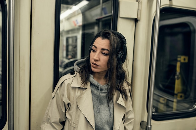 A girl in a beige trench coat rides in a subway car.