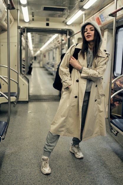 A girl in a beige trench coat rides in a subway car.