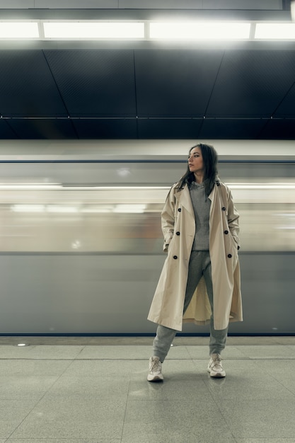 Girl in a beige trench coat in the subway waiting for the train on the platform