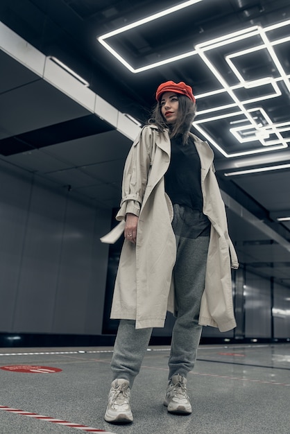 Girl in a beige trench coat in the subway waiting for the train on the platform