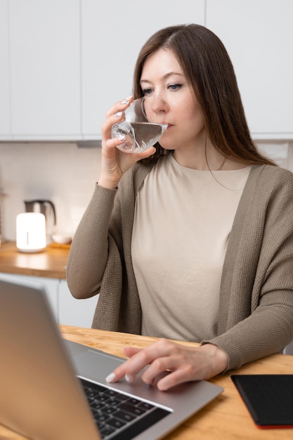 Girl in beige tshirt and grey jacket took a break from work and drinks water At the table laptop