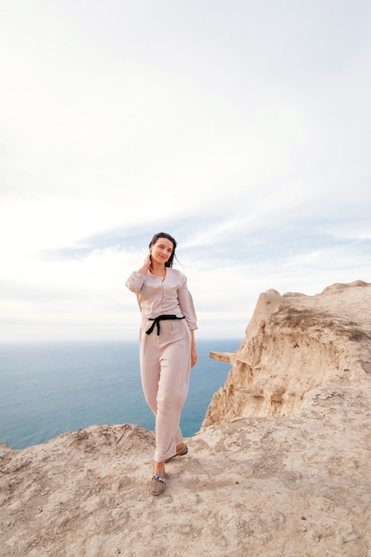 a girl in beige walks on a rock against the background of the sea