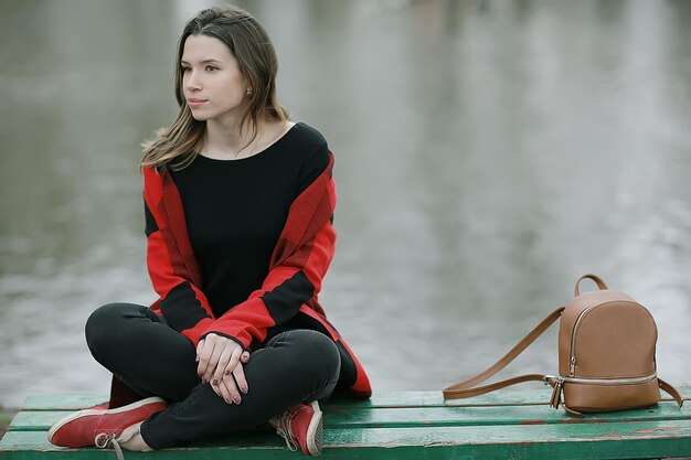 girl bench pond autumn / concept lonely girl in autumn relaxes near a pond on a garden bench, autumn landscape