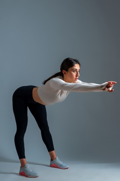 Girl bending body forward with outstretched arms on grey wall