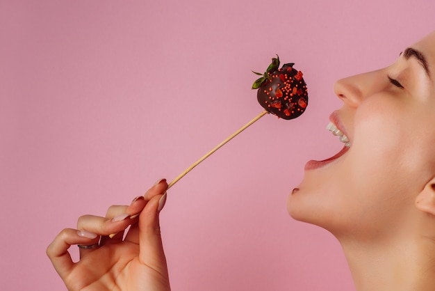 A girl bites a chocolate covered strawberry