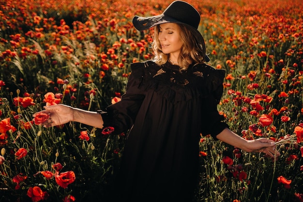 A girl in a black dress and hat on a poppy field at sunset