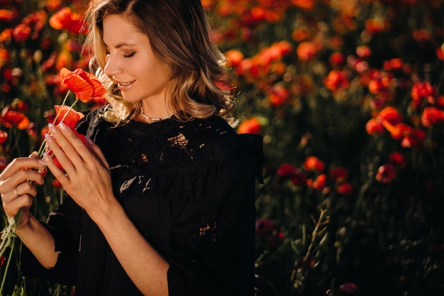 A girl in a black dress on a poppy field at sunset