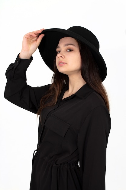 A girl in a black hat poses and smiles on a white background holding her hat