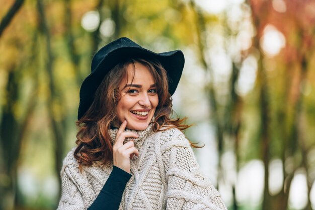 A girl in a black hat with a charming smile stands in the park