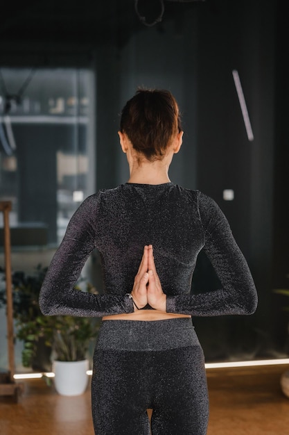 A girl in a black sports uniform does yoga standing on a mat in the gym