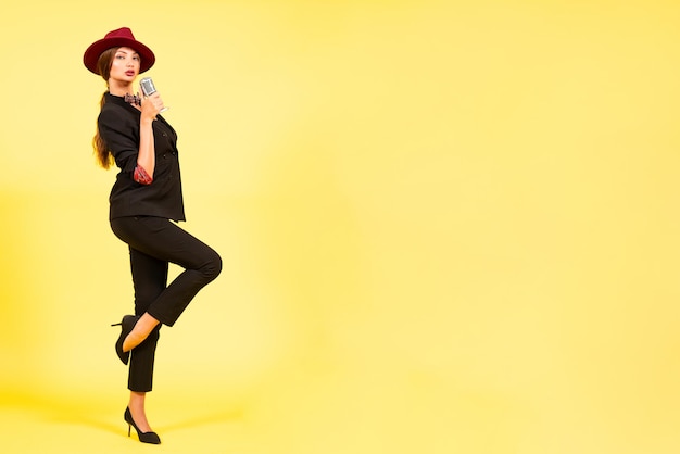 Girl in a black suit on a yellow background sings in a retro microphone portrait music full growth