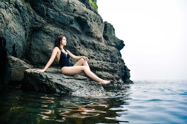 Girl in a black swimsuit in the sea near volcanic dark rocks